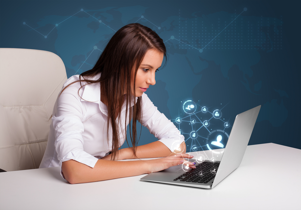 Beautiful young lady sitting at desk and typing on laptop with social network icons comming out-1